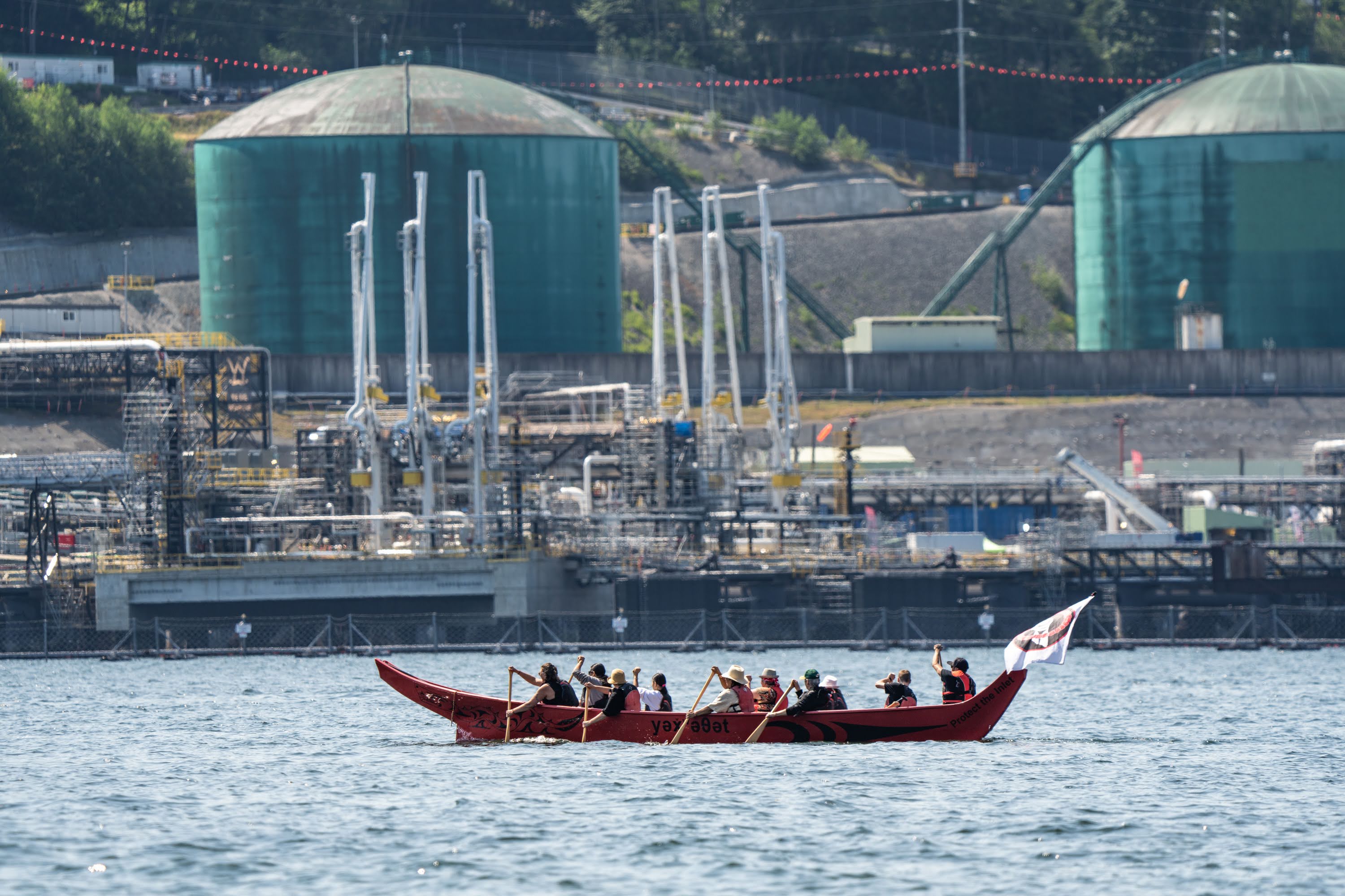 Tsleil-Waututh Nation members paddling in a canoe in front of the Trans Mountain oil pipeline terminal in Burrard Inlet, Burnaby.